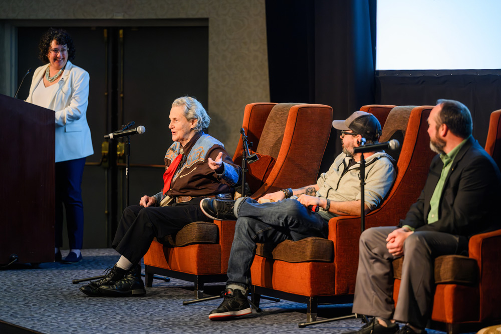 small group of people sitting on chairs on a stage during a panel