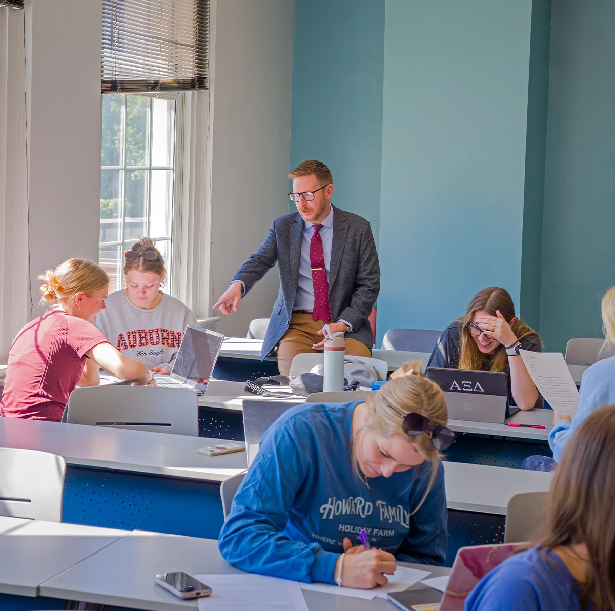 An Auburn University professor in a grey blazer and red tie assisting a group of students during an Agricultural Communications class.