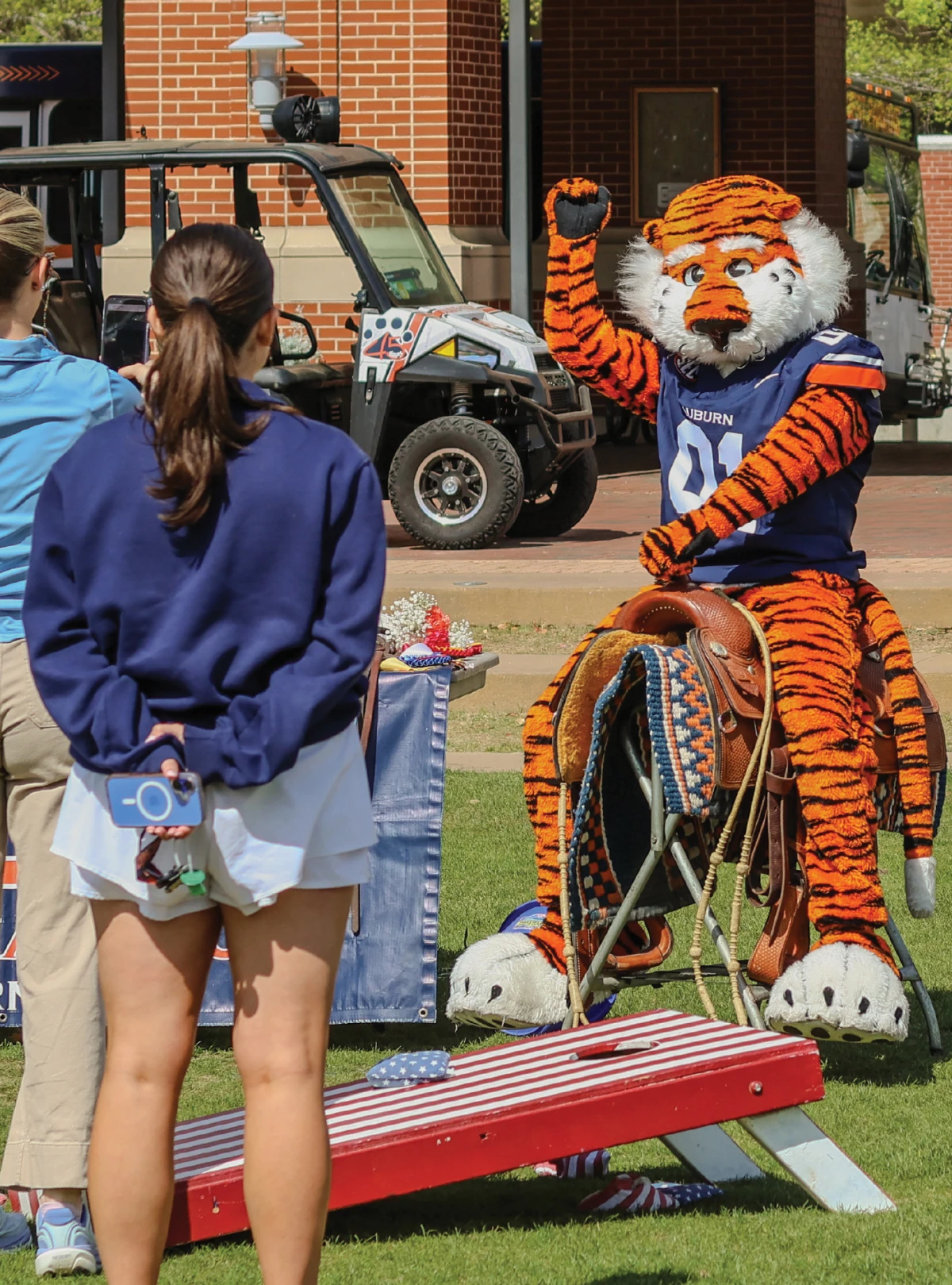 Aubie waves while seated on a saddle at an Auburn campus event.