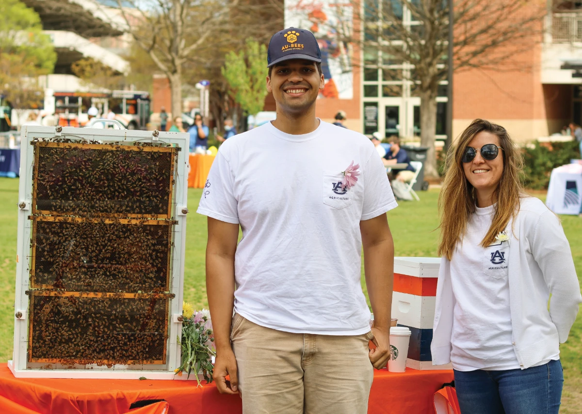 Auburn Agriculture representatives standing beside a live beehive display at a campus event.