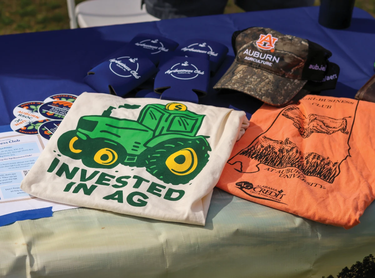 Auburn Agriculture club merchandise displayed on a table, including shirts, hats, stickers, and drink sleeves.